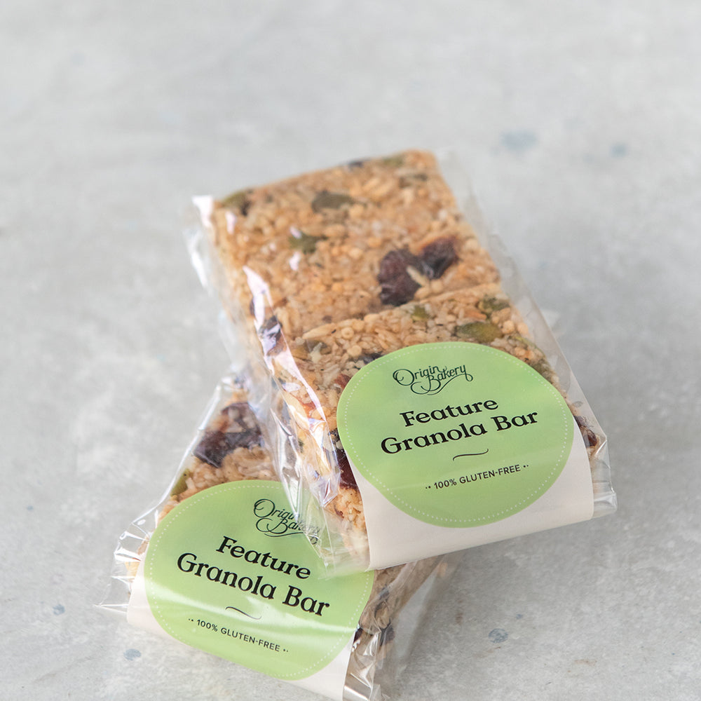 
                      
                        stack of 2 gluten free granola bar packs, 2 squares in each compostable cellulose bag with Origin Bakery sticker
                      
                    