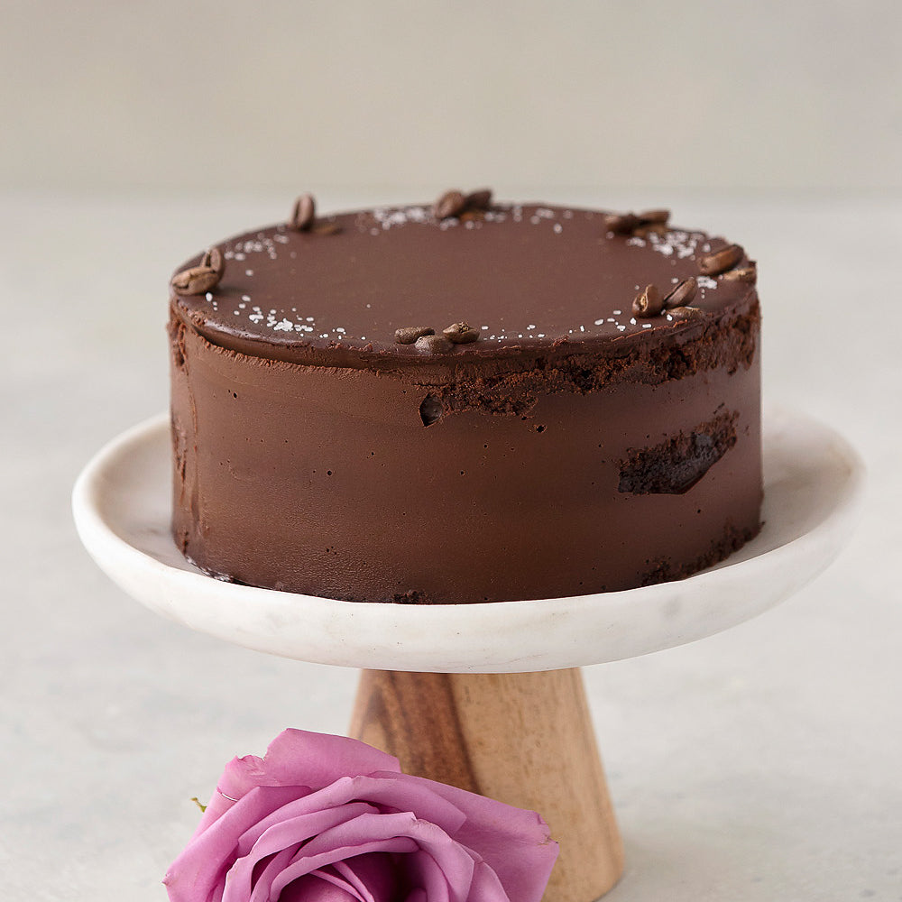 gluten free Vegan Ganache chocolate cake with vanilla sea salt and coffee bean garnish, displayed on cake stand with rose