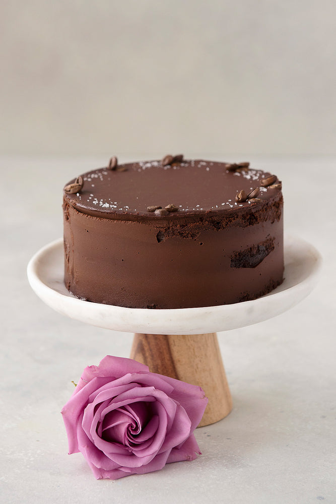 gluten free Vegan Ganache chocolate cake with vanilla sea salt and coffee bean garnish, displayed on cake stand with rose