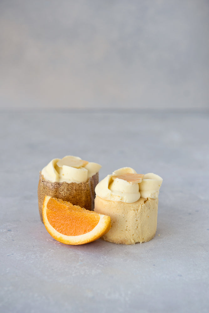 2 gluten free orange creamsicle mini cheesecakes, one in panettone wrapper one unwrapped with slice orange
