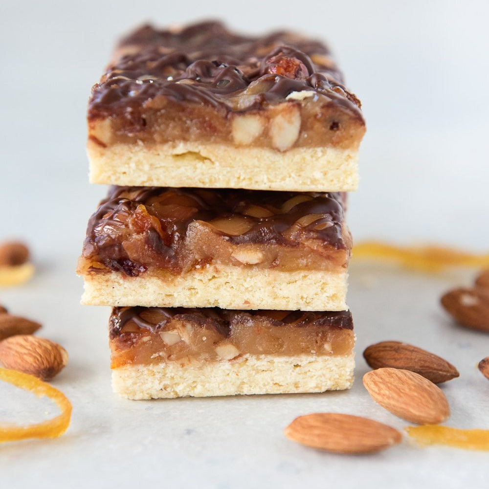 vertical stack 3 gluten free florentine bars made with caramel almonds candied citrus cranberry and chocolate drizzle on shortcrust pastry base