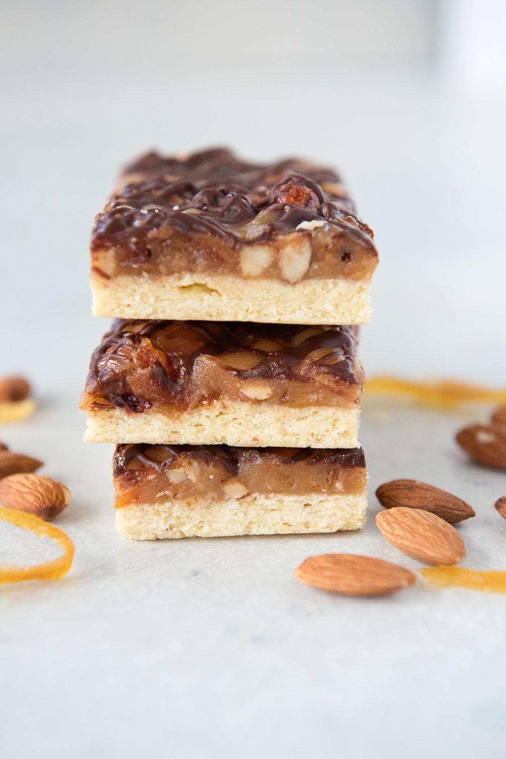 vertical stack 3 gluten free florentine bars made with caramel almonds candied citrus cranberry and chocolate drizzle on shortcrust pastry base
