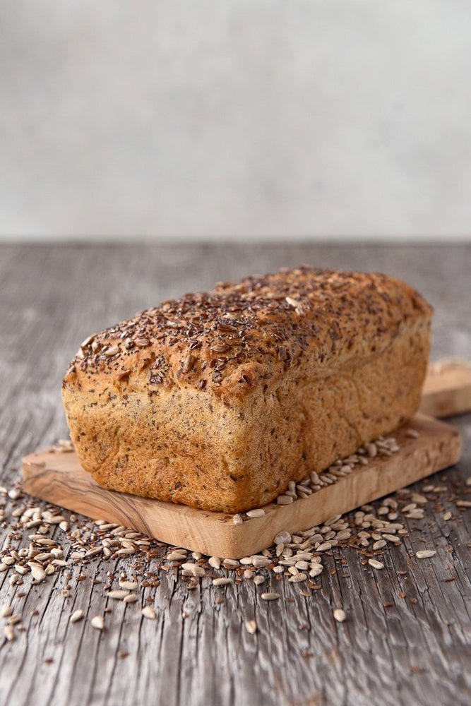 whole loaf gluten free Harvest multigrain sandwich bread on wood board, displayed with sunflower, flax and poppy seeds