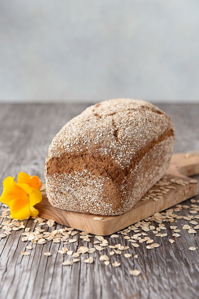 whole loaf gluten free Oat Bread on board shown with oats and flower