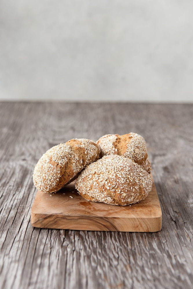 3 gluten free oat bread dinner rolls piled on wood cutting board