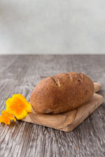 whole loaf gluten free Multigrain Sourdough on wood board with flower