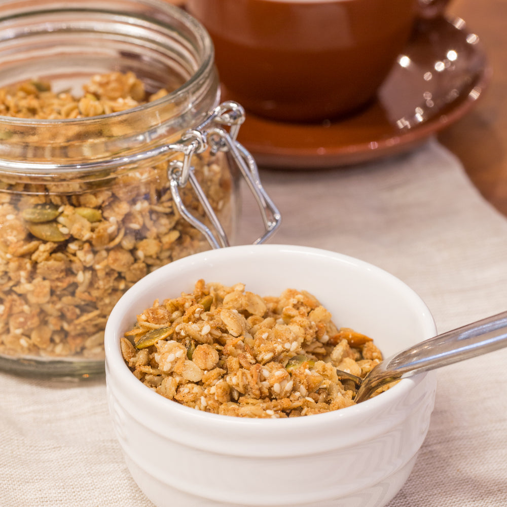 gluten free butter granola in white bowl with spoon, displayed with latte and jar granola