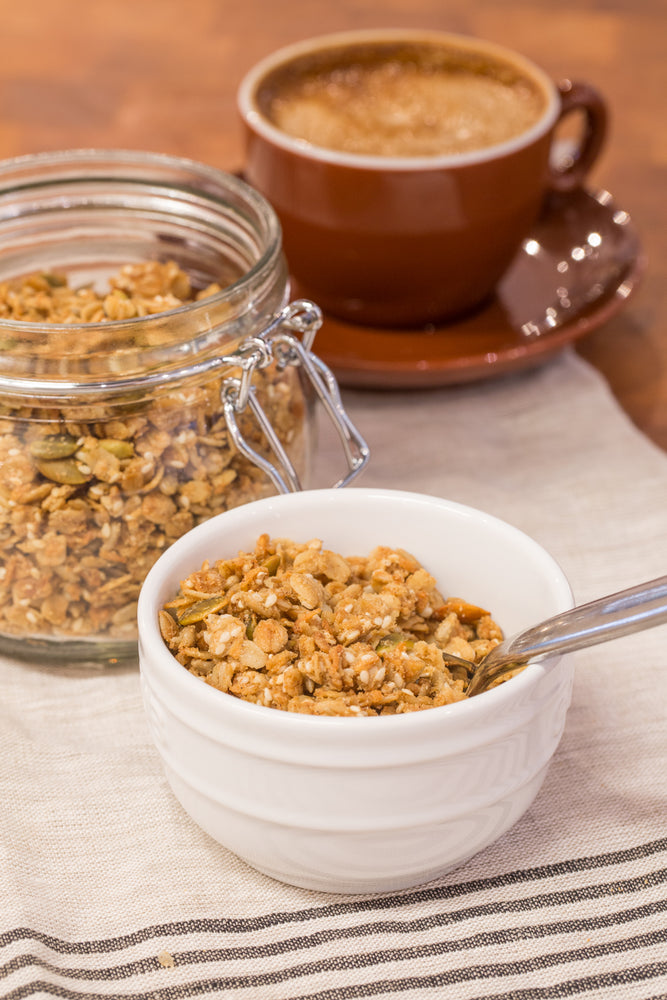 gluten free butter granola in white bowl with spoon, displayed with latte and jar granola